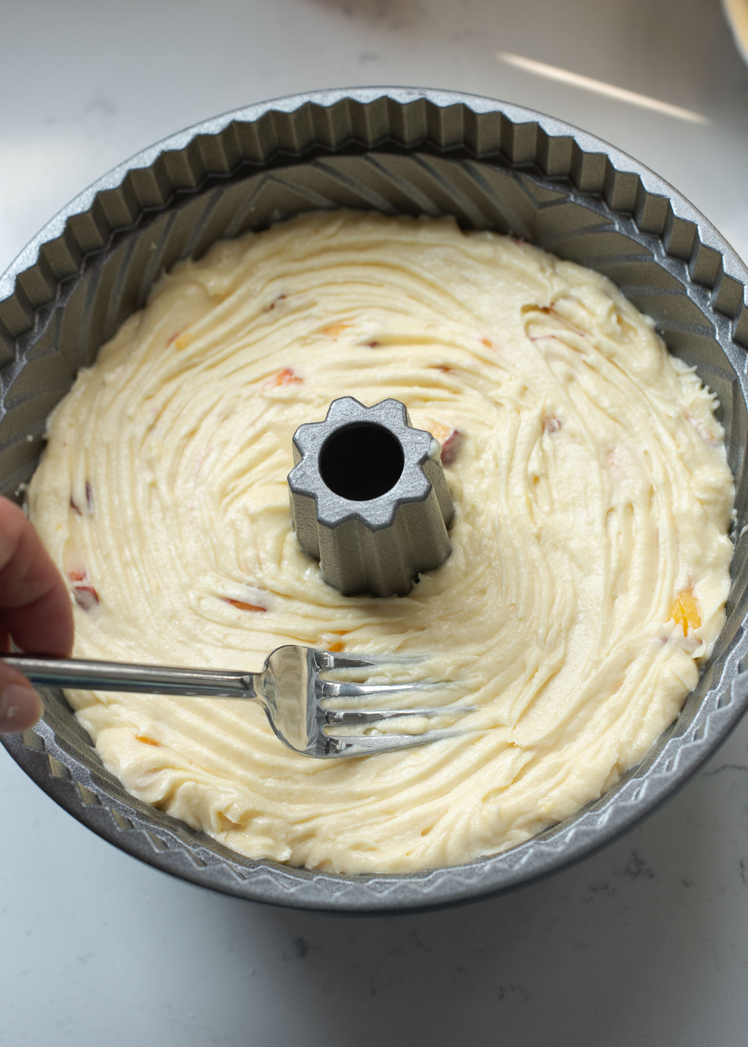 A fork is smoothing the top of peach pound cake batter in a bundt pan.