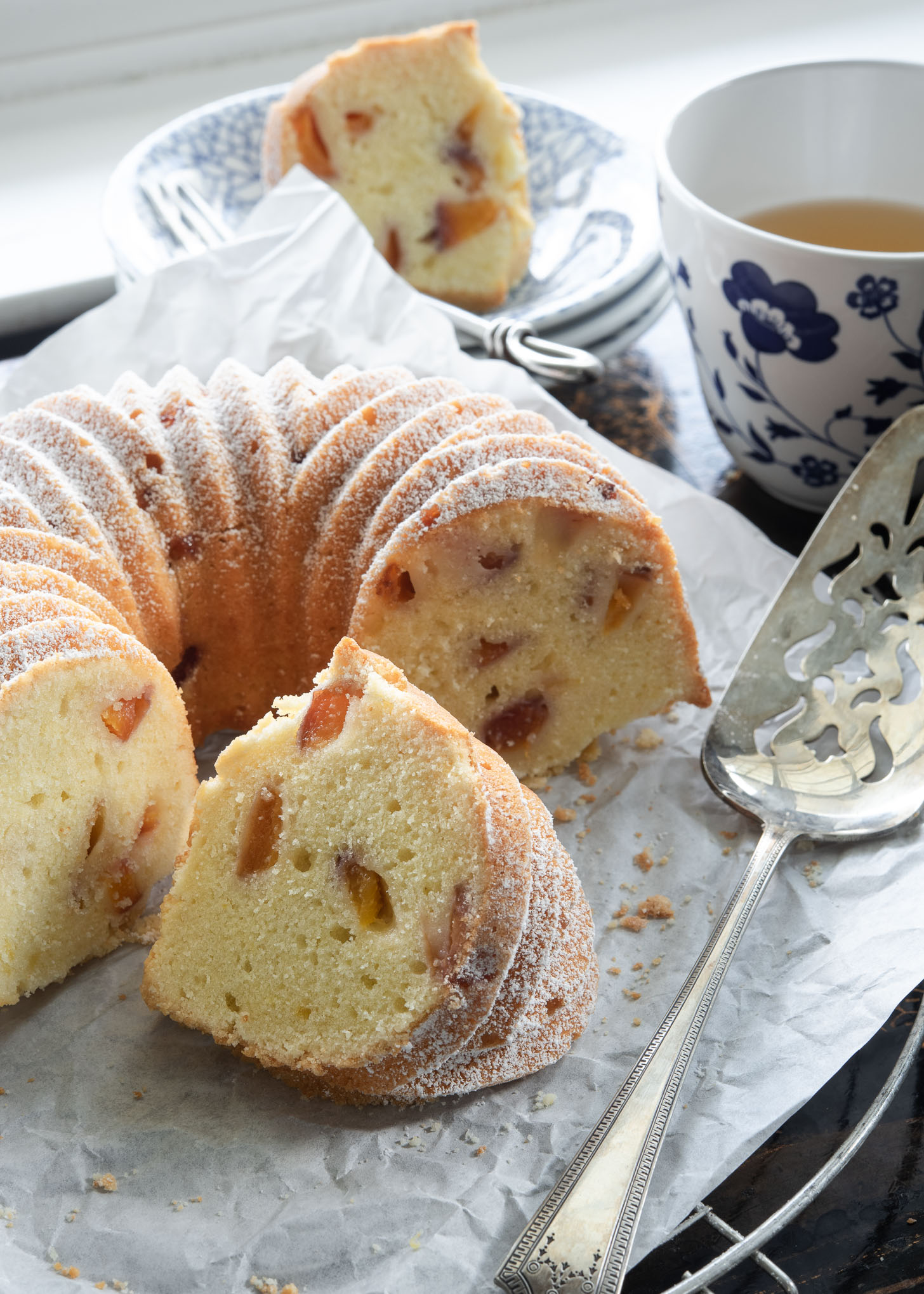 Peach pound cake baked in a bundt pan is dusted with powdered sugar and sliced.