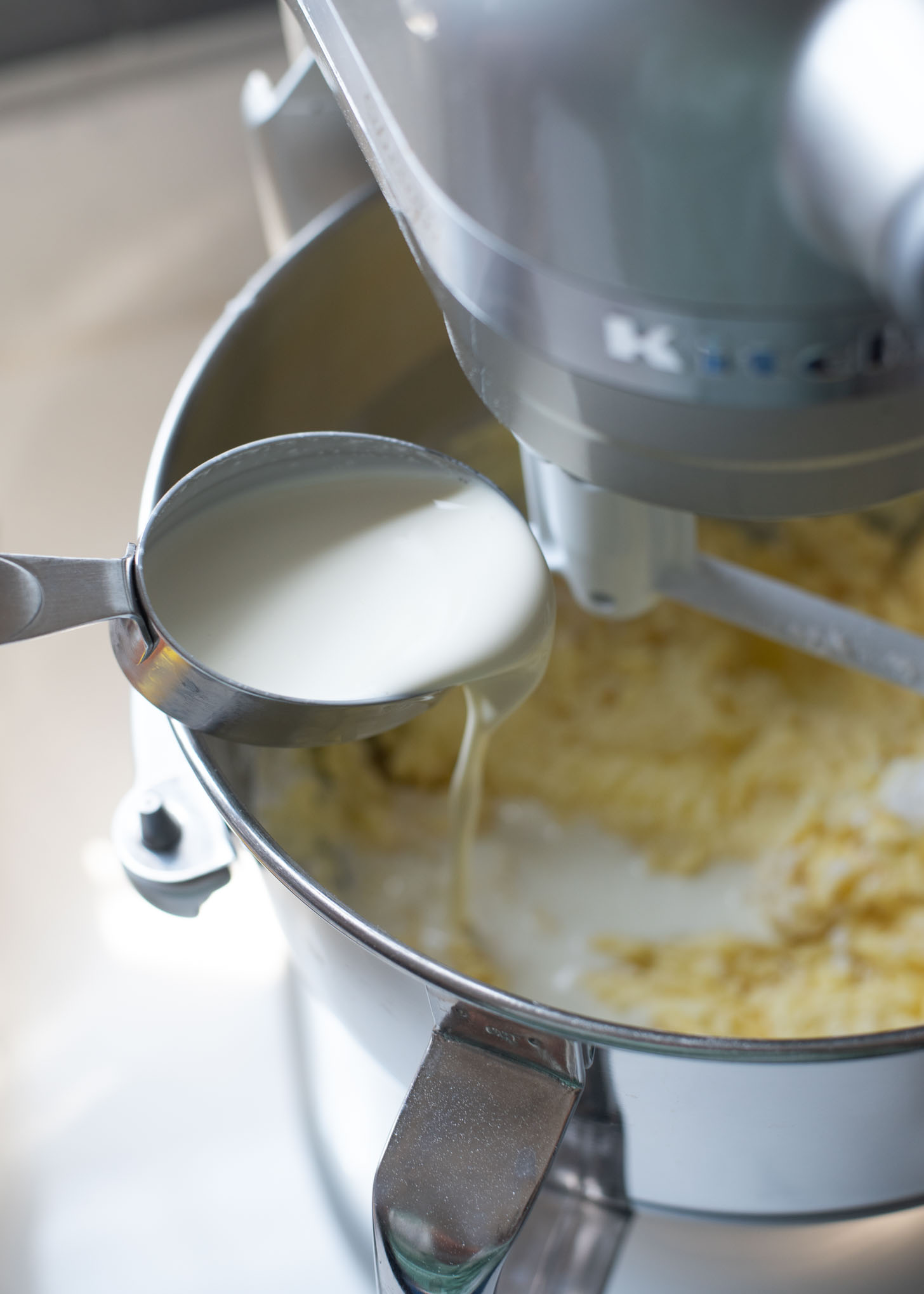 Heavy cream is added to flour mixture of peach pound cake in a mixer.