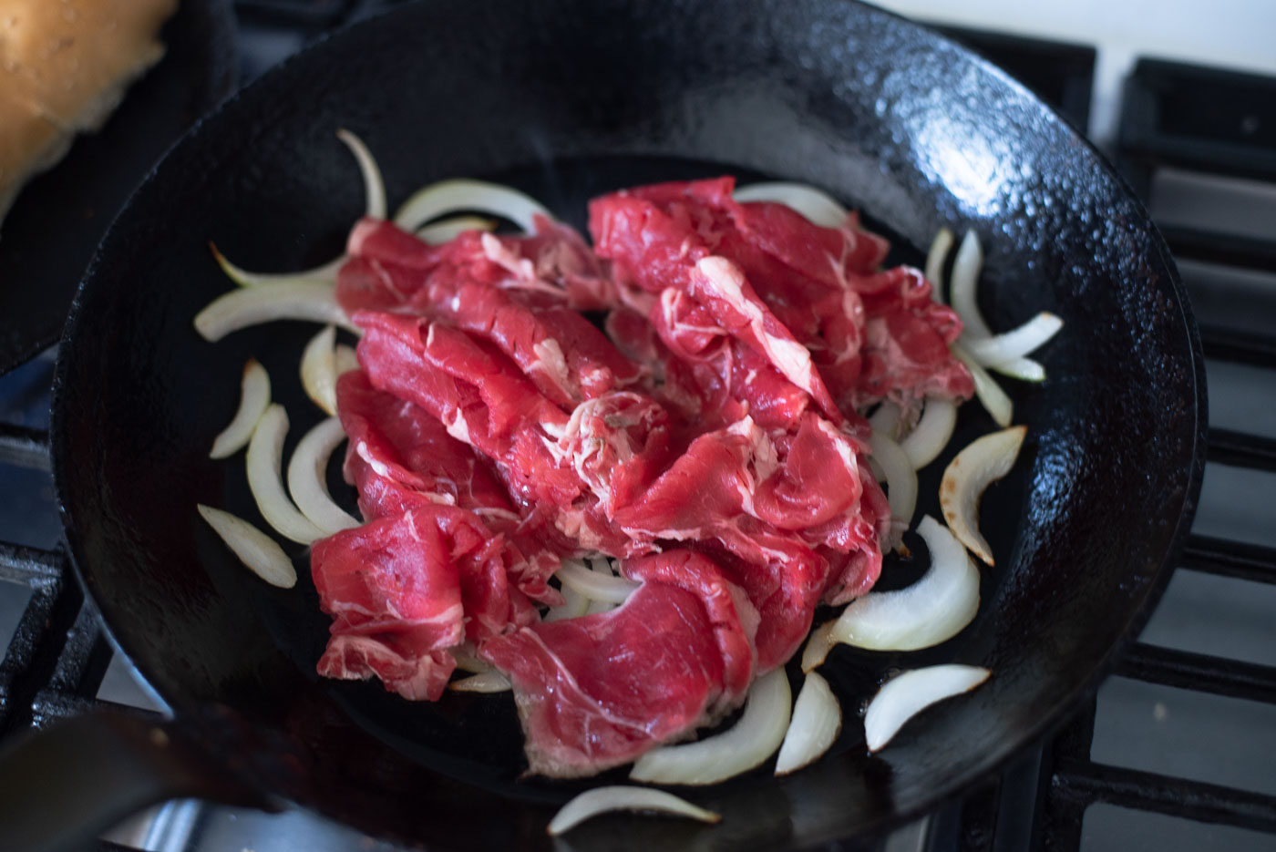 Onion and thin beef slices are cooking in a skillet.