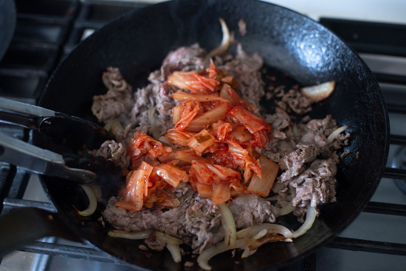 Kimchi slices are added to cooked beef and onion in a skillet for bulgogi cheesesteak.