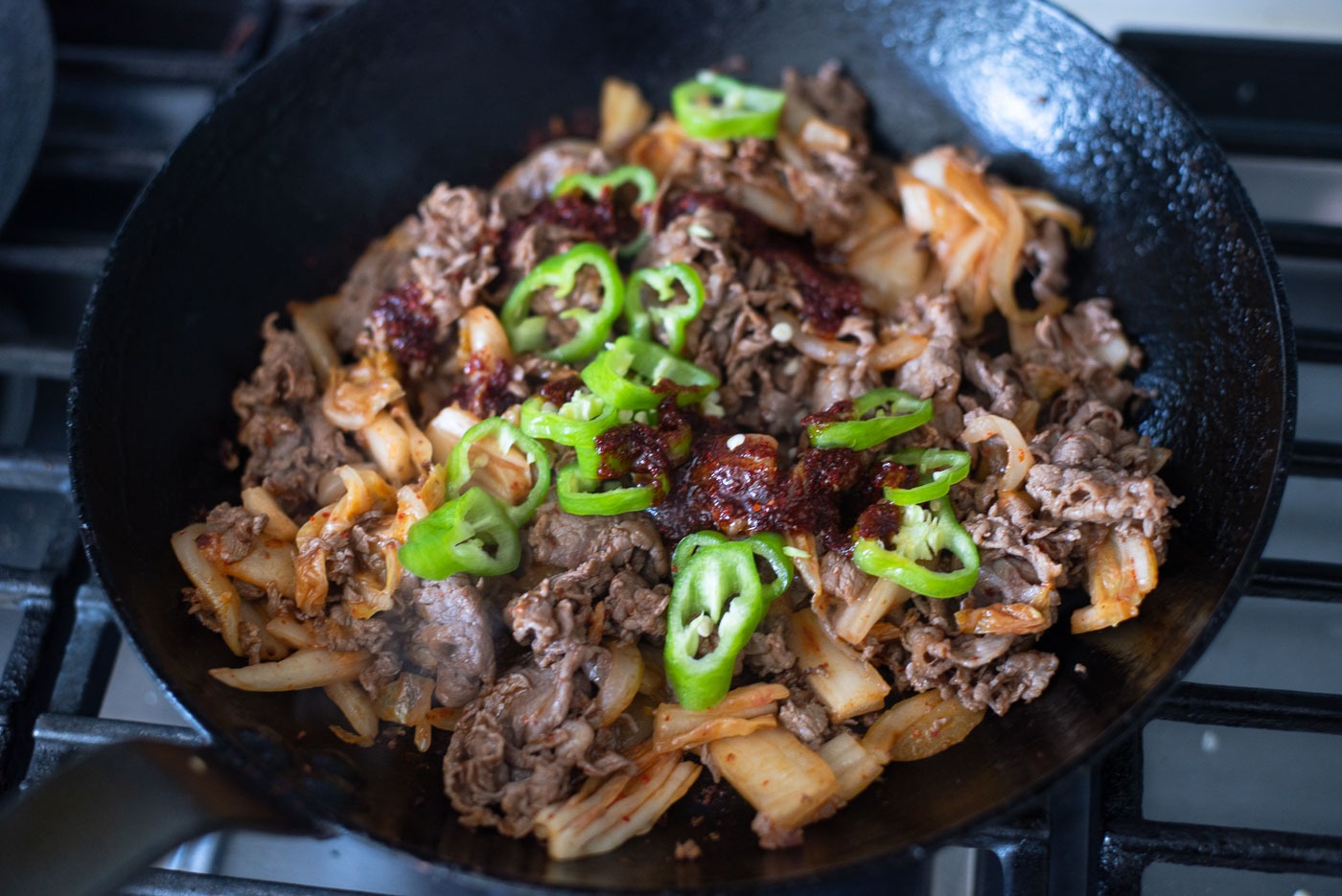 Fresh green chili slices are added bulgogi kimchi mixture in a skillet.