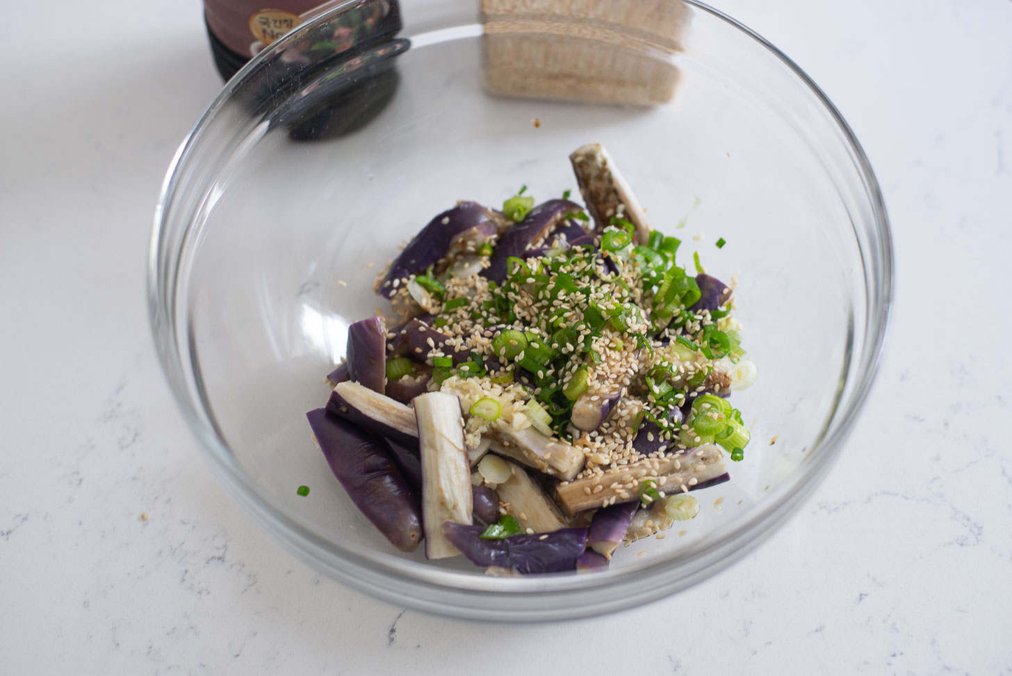 Korean eggplant side dish seasonings are added to steamed eggplants in a bowl.