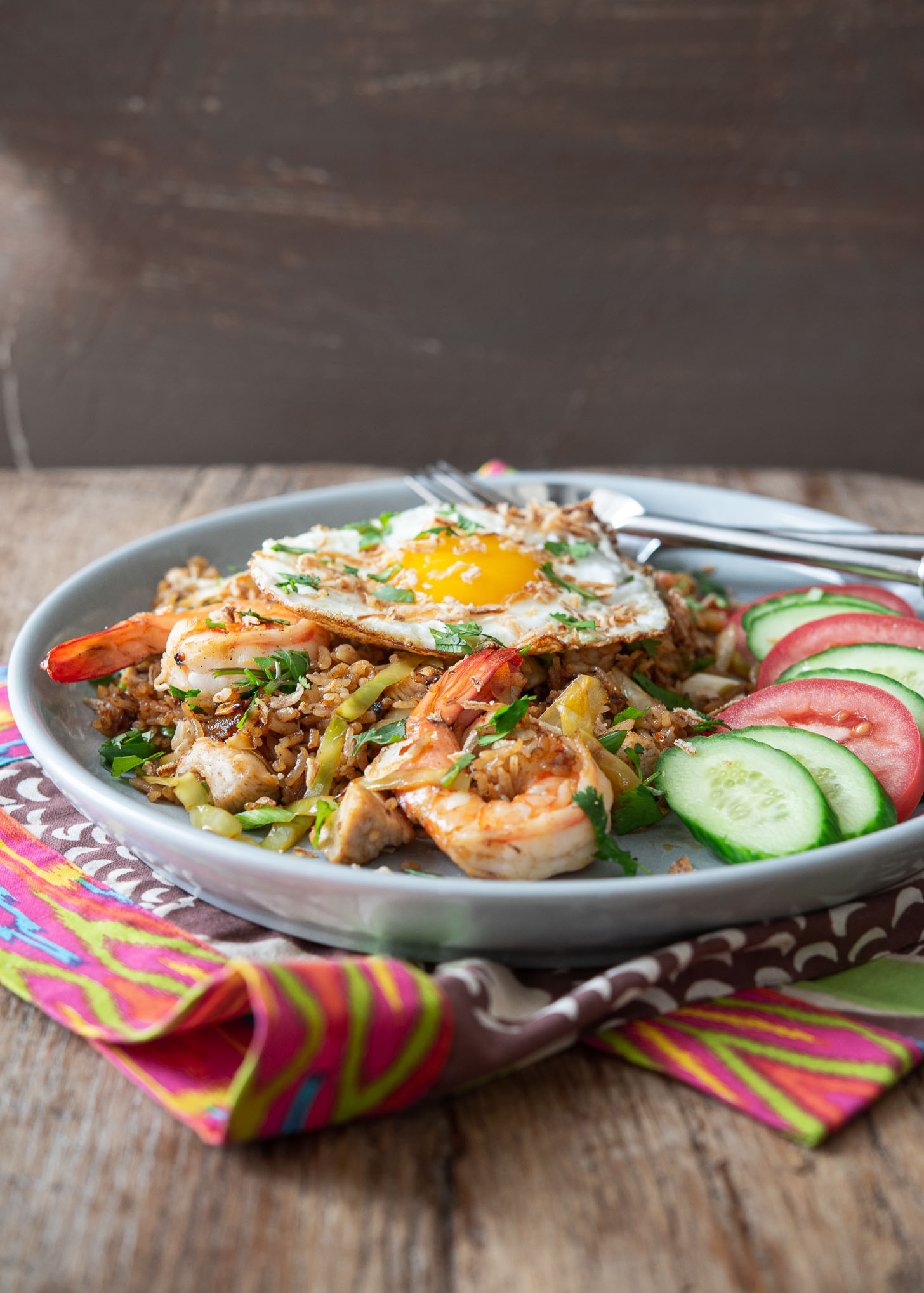 Indonesian fried rice (Nasi Goreng) is served with cucumber and tomato slices in a plate.