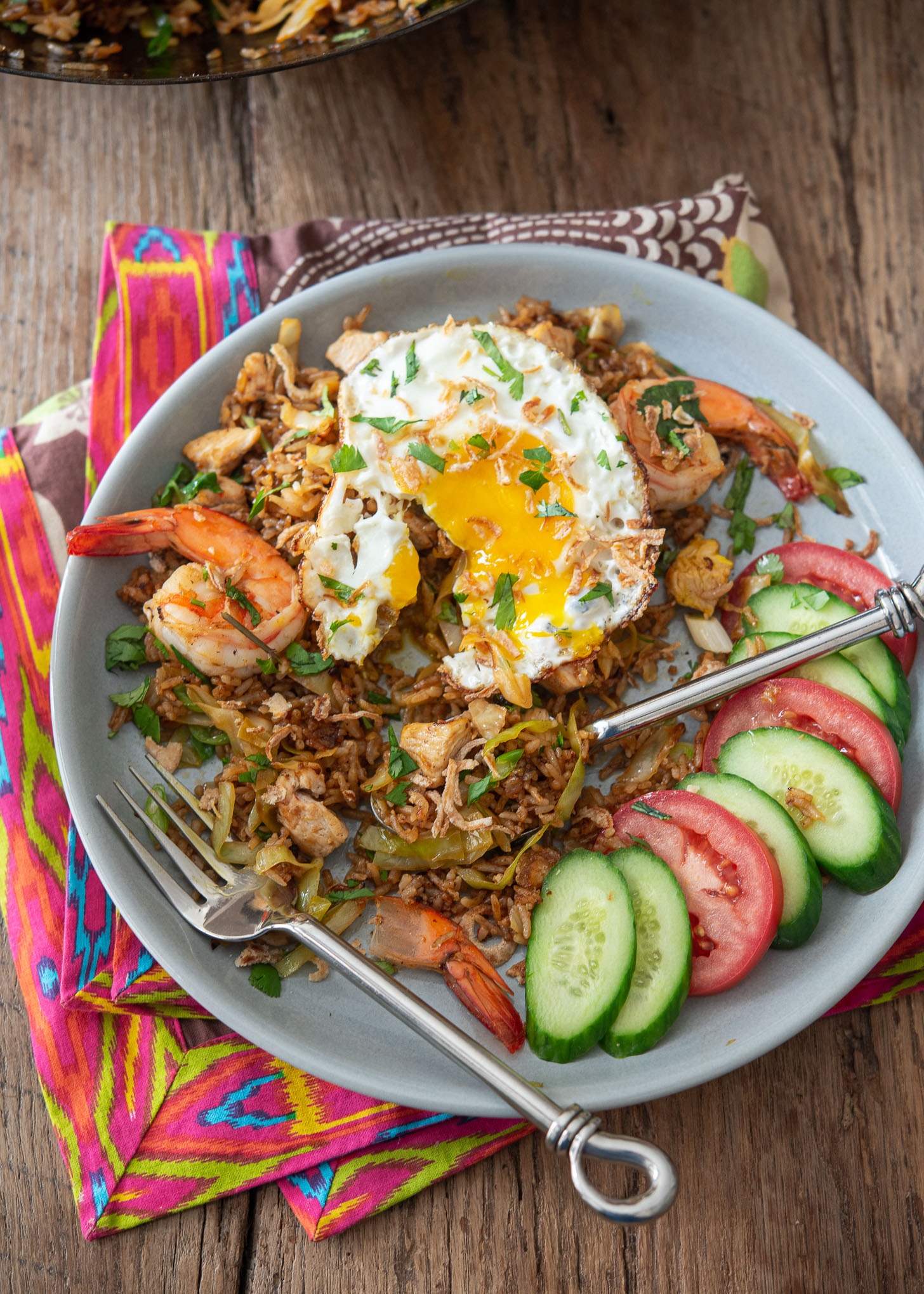 Nasi goreng is topped with a fried egg and served with cucumber and tomato.