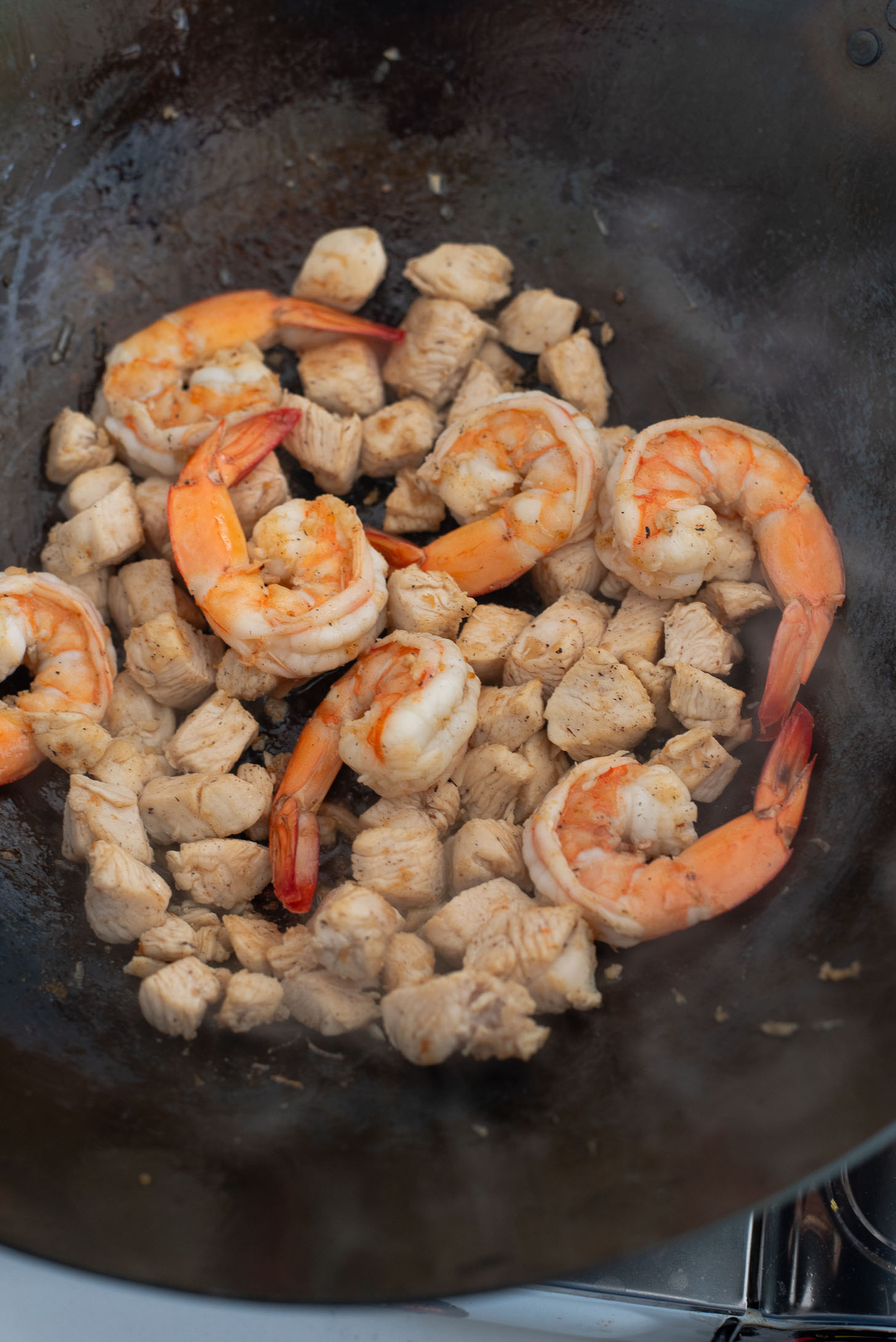Chicken and shrimp are stir fried in a wok.