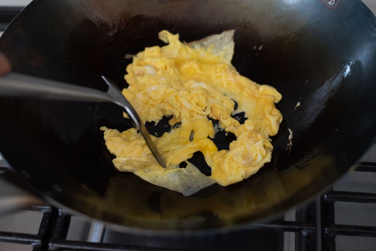 Egg is scrambled in a wok to make Spam fried rice.