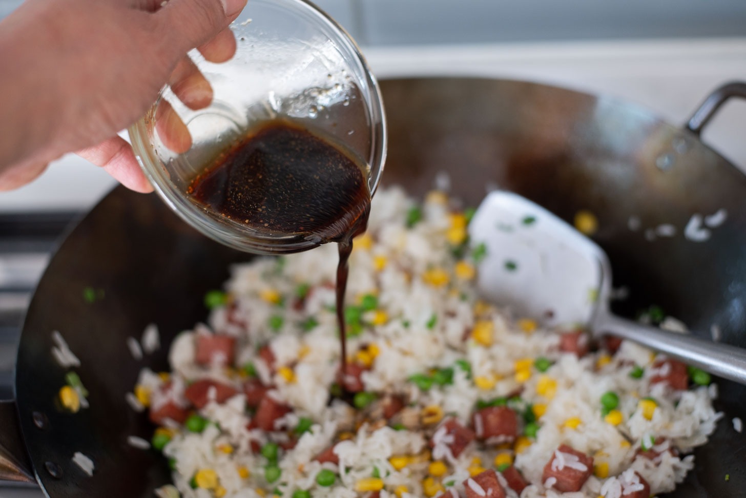 Spam fried rice sauce is added to fried rice in a wok.