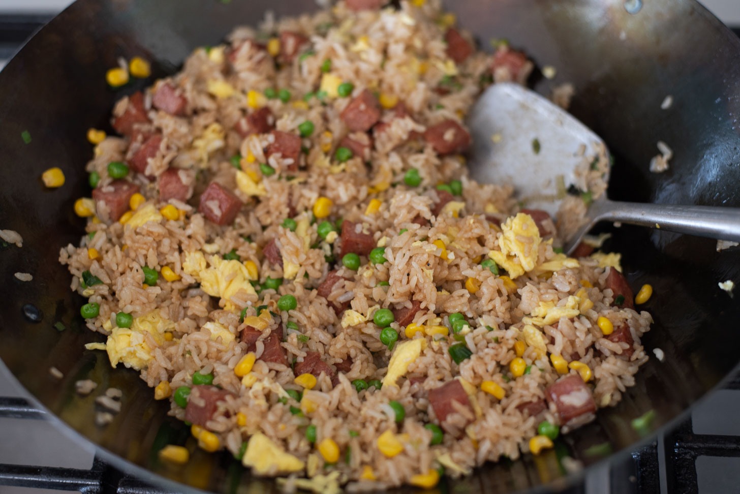 Scrambled eggs are added to Spam fried rice at the end of cooking.