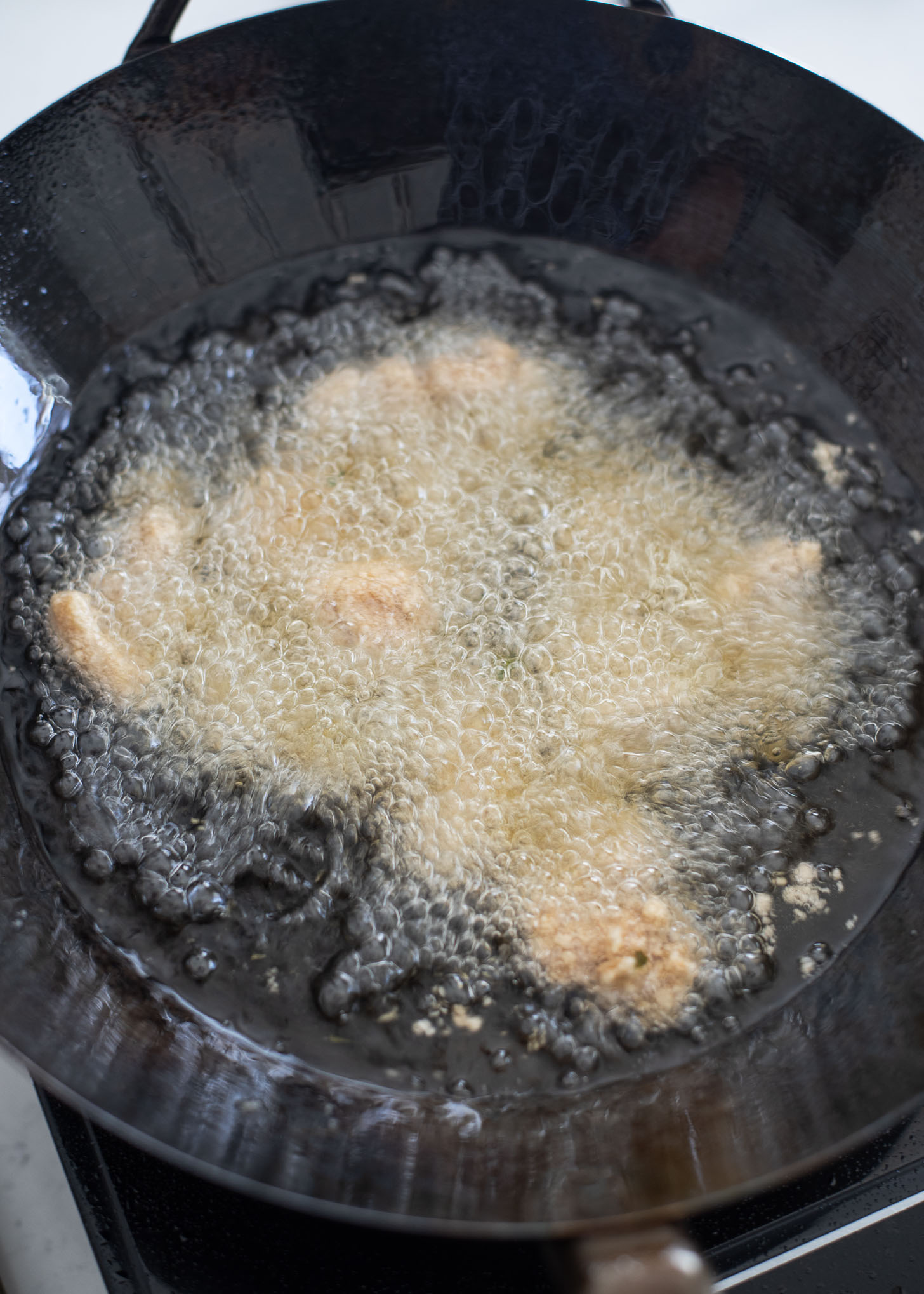 Chicken pieces are deep frying in hot oil in a wok.