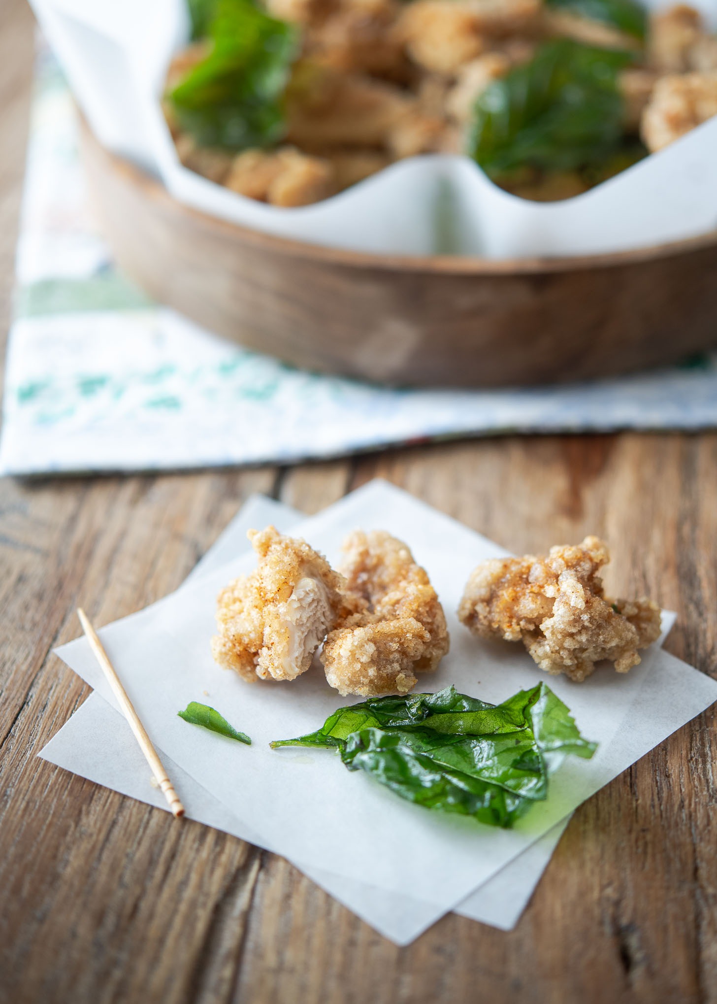 A few pieces of Taiwanese popcorn chicken and fried basil placed on a parchment paper.