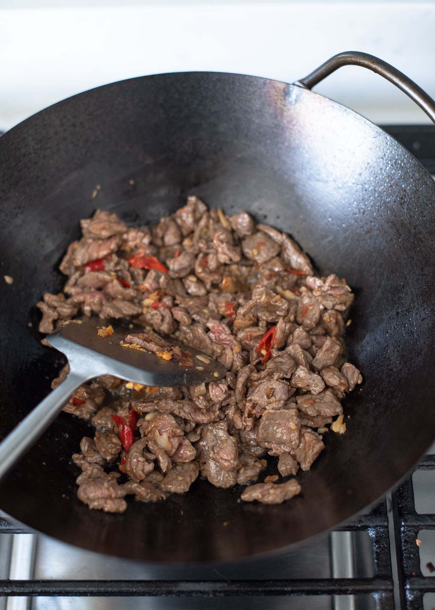 Beef pieces are added to wok to make Thai basil beef stir-fry.