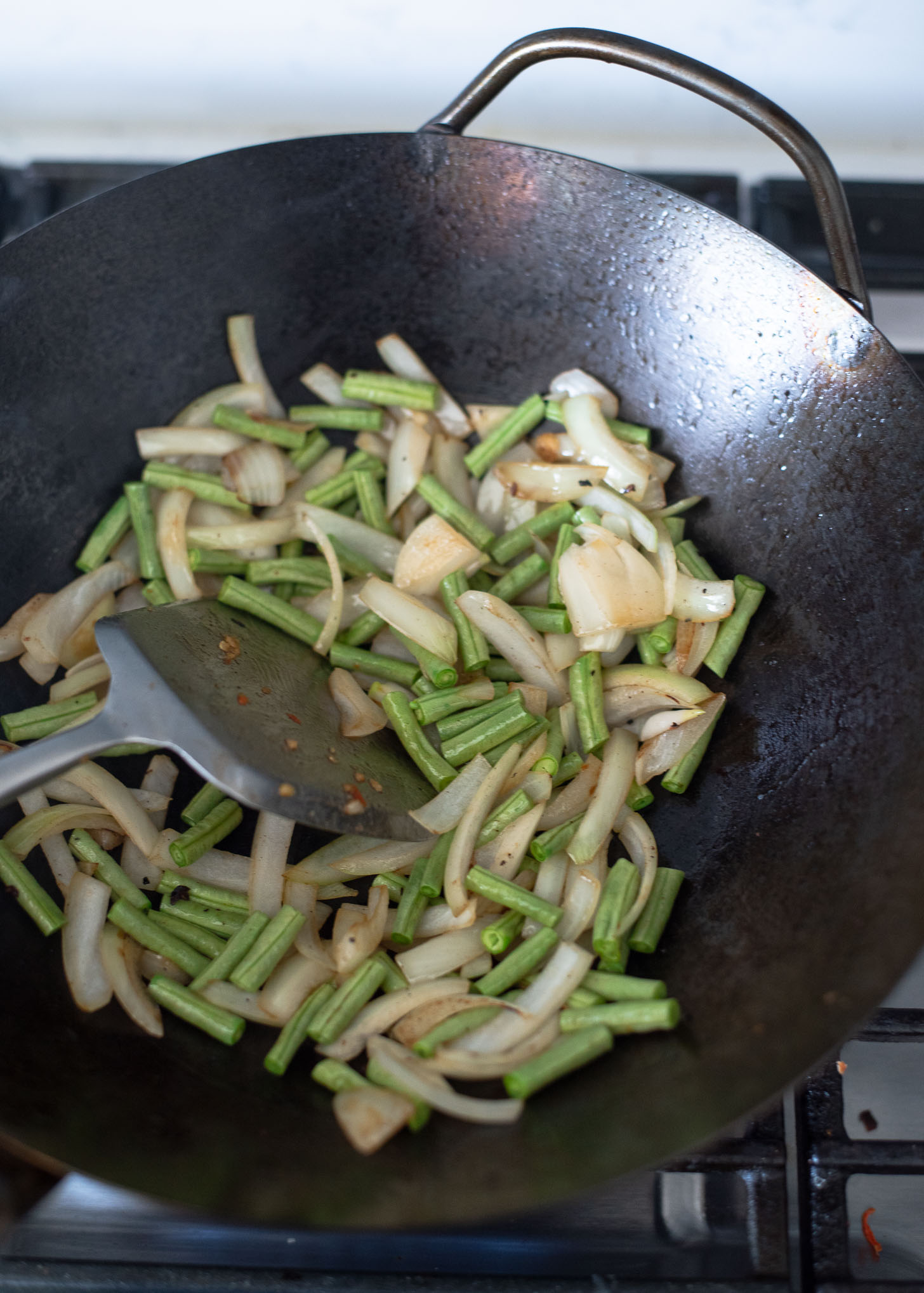 Onion and long bean slices are stir frying in a wok to make Thai basil beef.