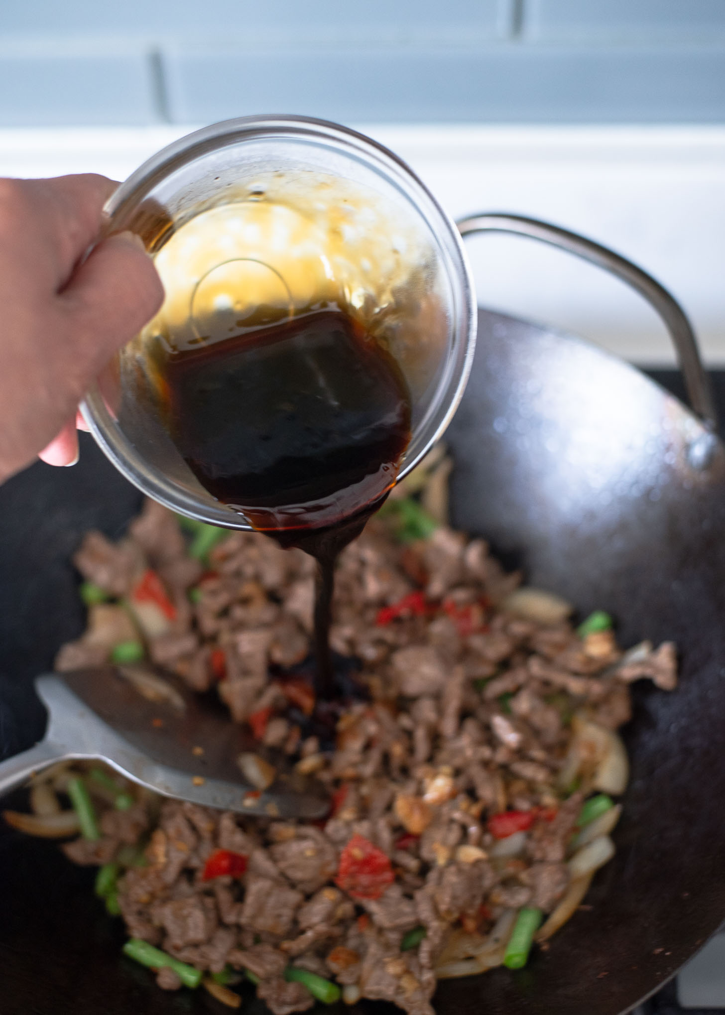 Thai basil beef sauce is added to the beef stir fry in a wok.