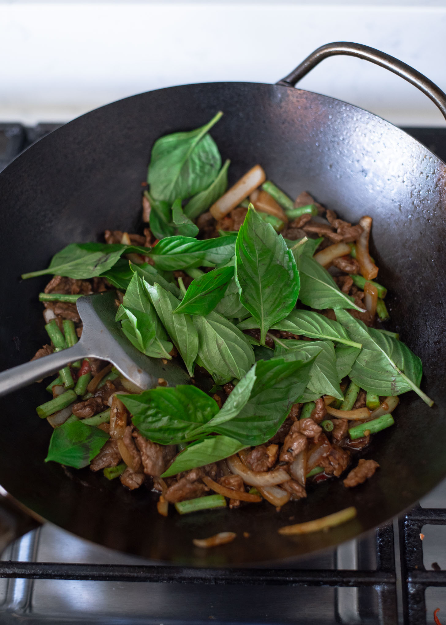 Thai basil leaves are added to the beef stir fry in a wok.