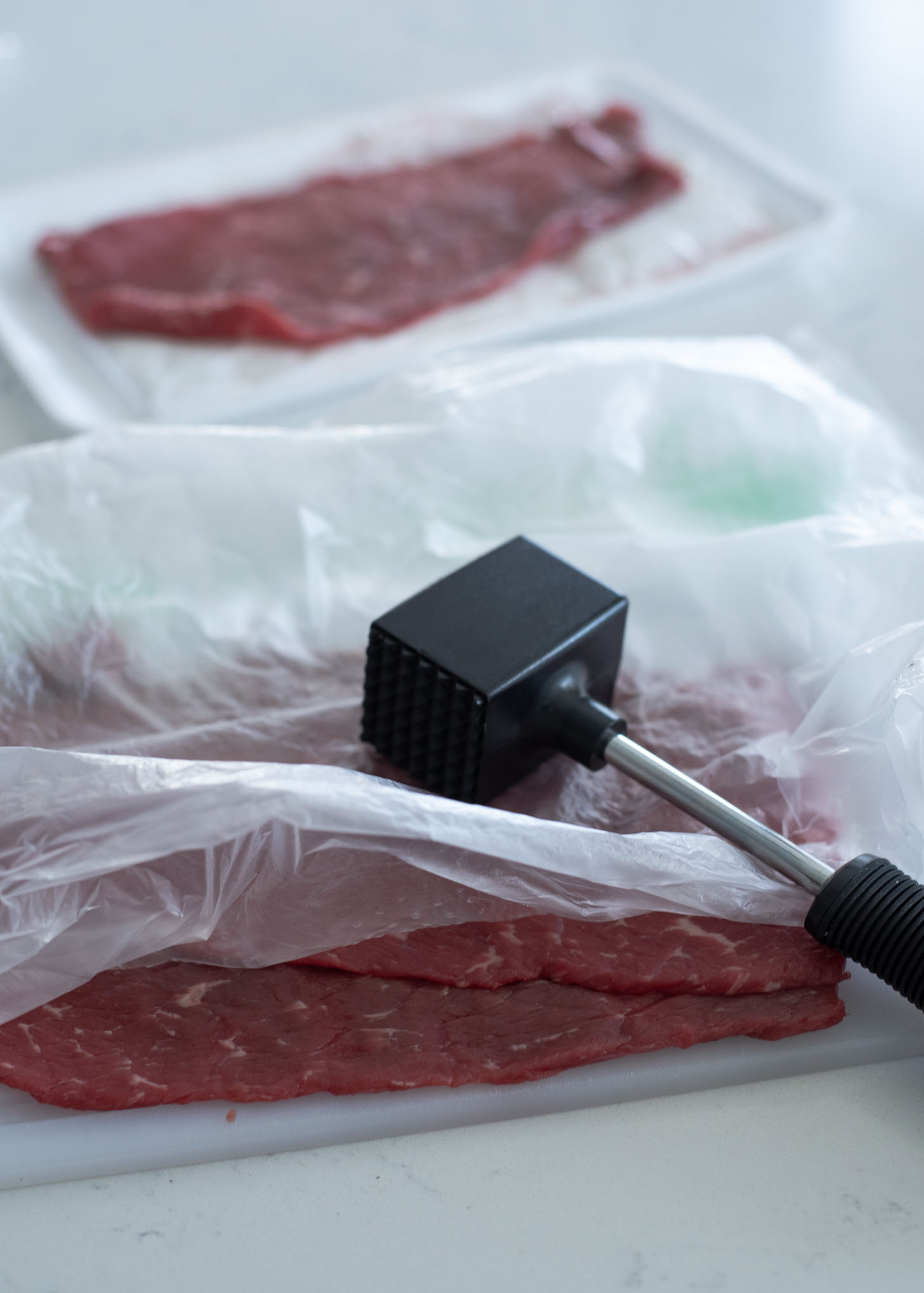 Beef slices are covered with a plastic and pounded by a meat hammer.