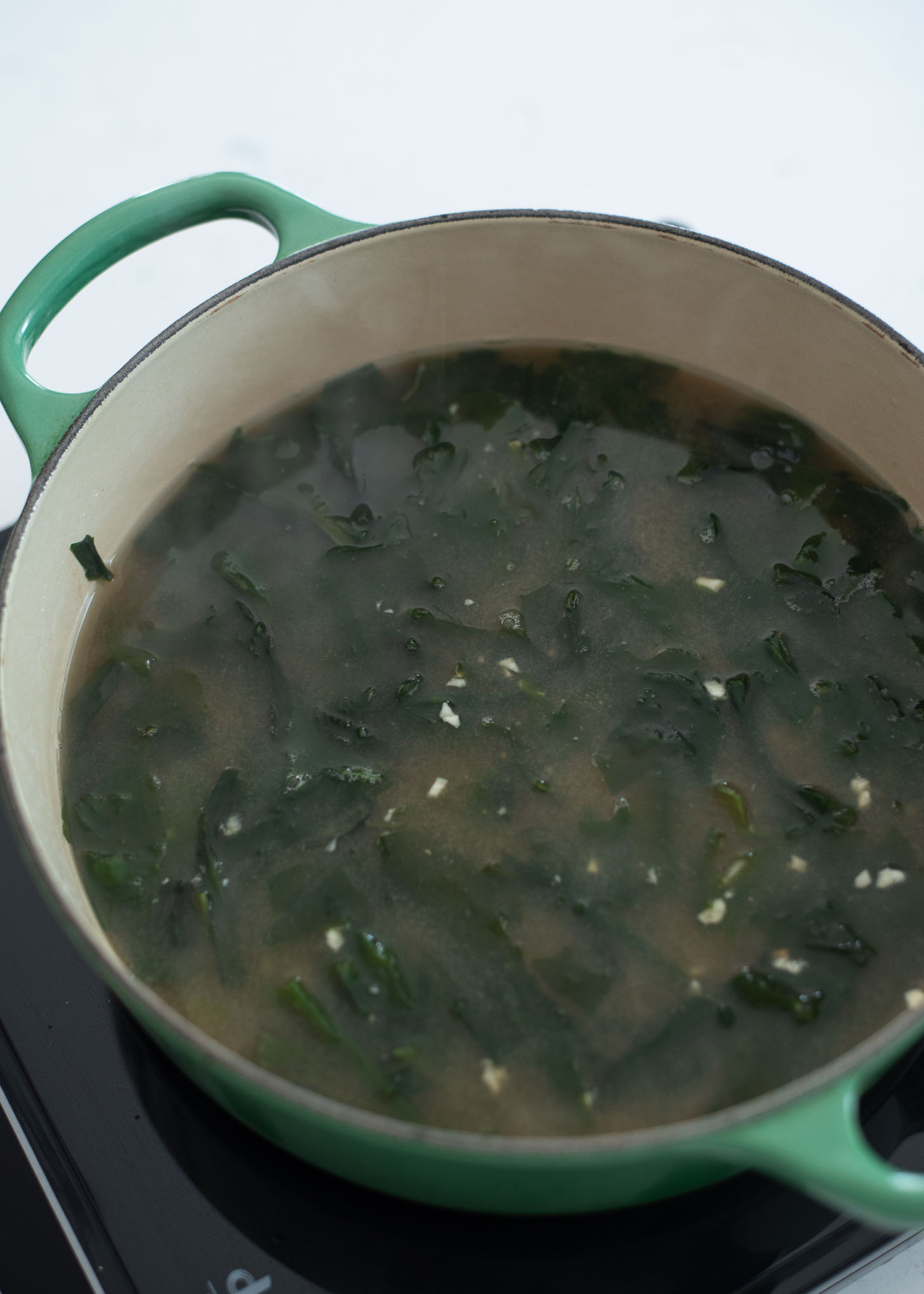 Chopped seaweed is added to the soup base in a pot.