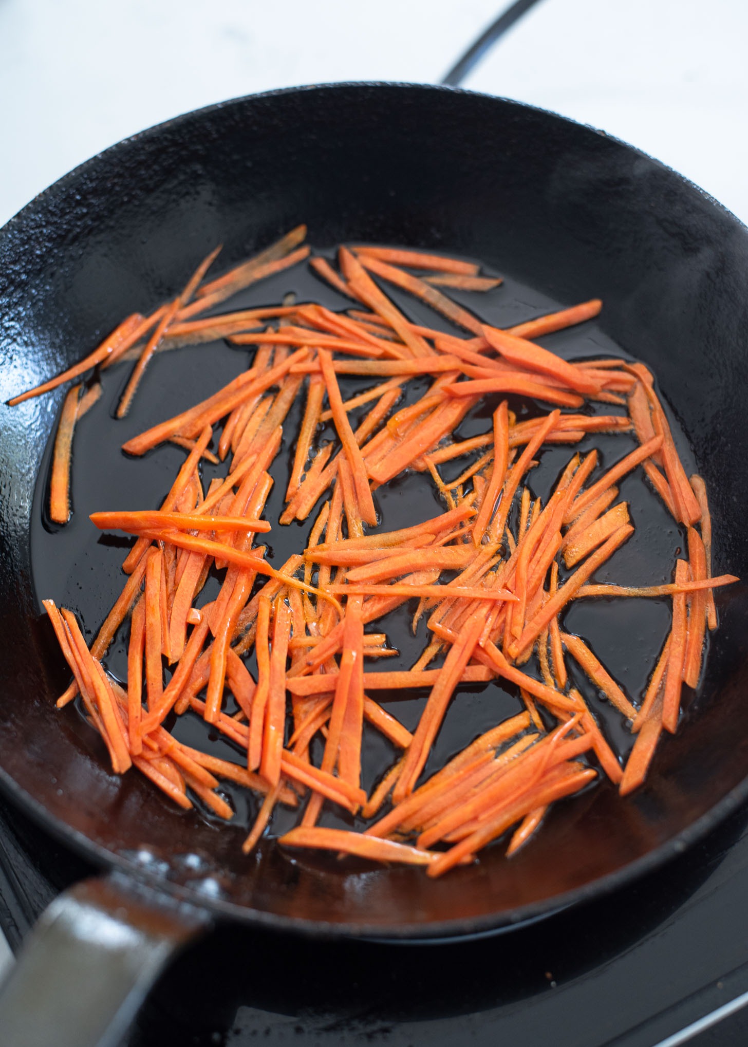 Shredded carrots are stir frying in a skillet. 