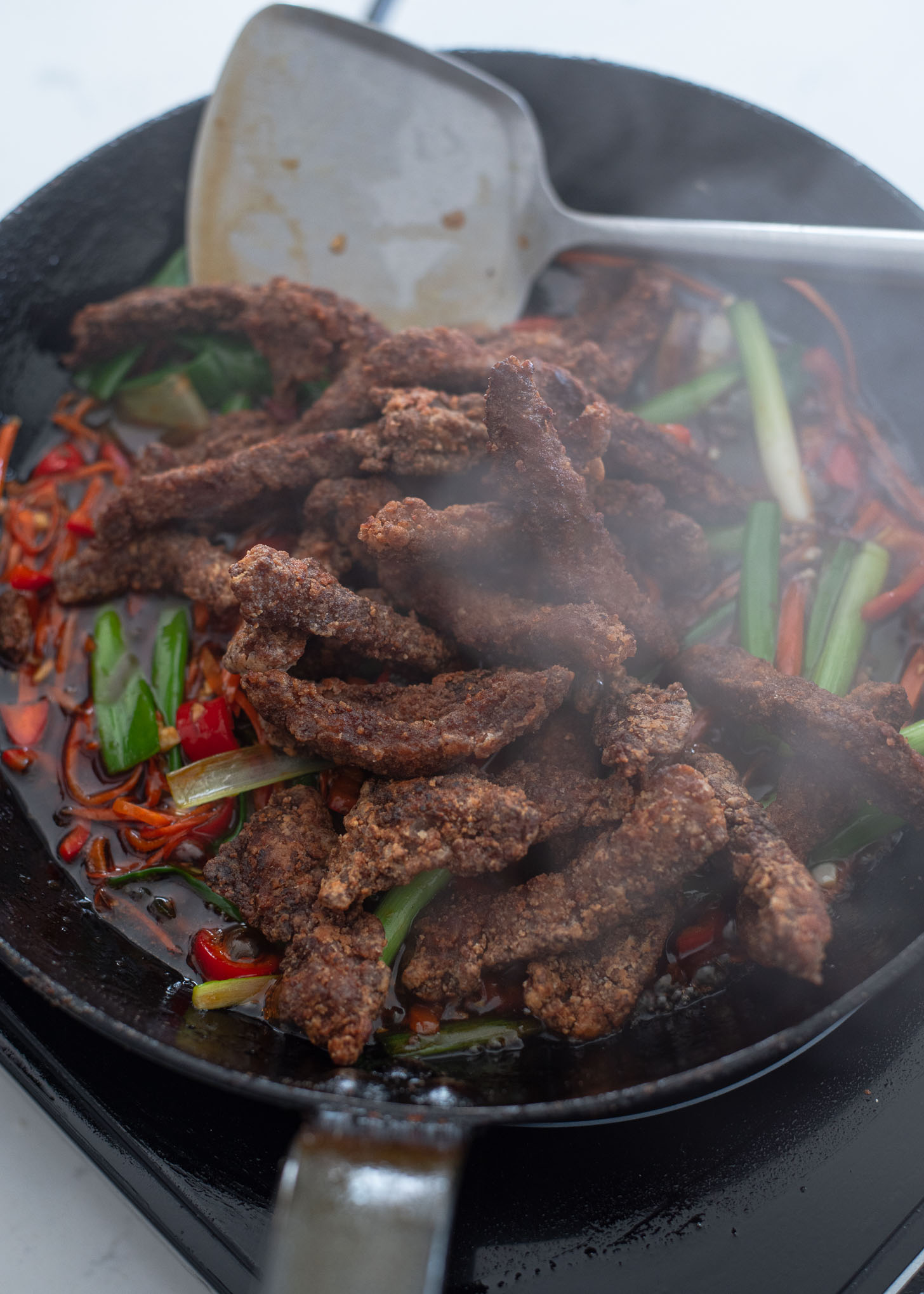 Add crispy beef strips to the sauce and vegetables in a skillet.