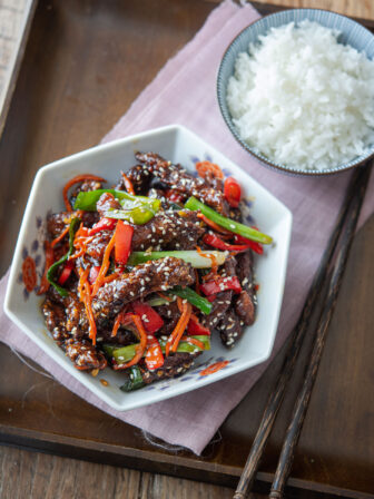 A bowl of Chinese crispy beef is served with rice on a tray