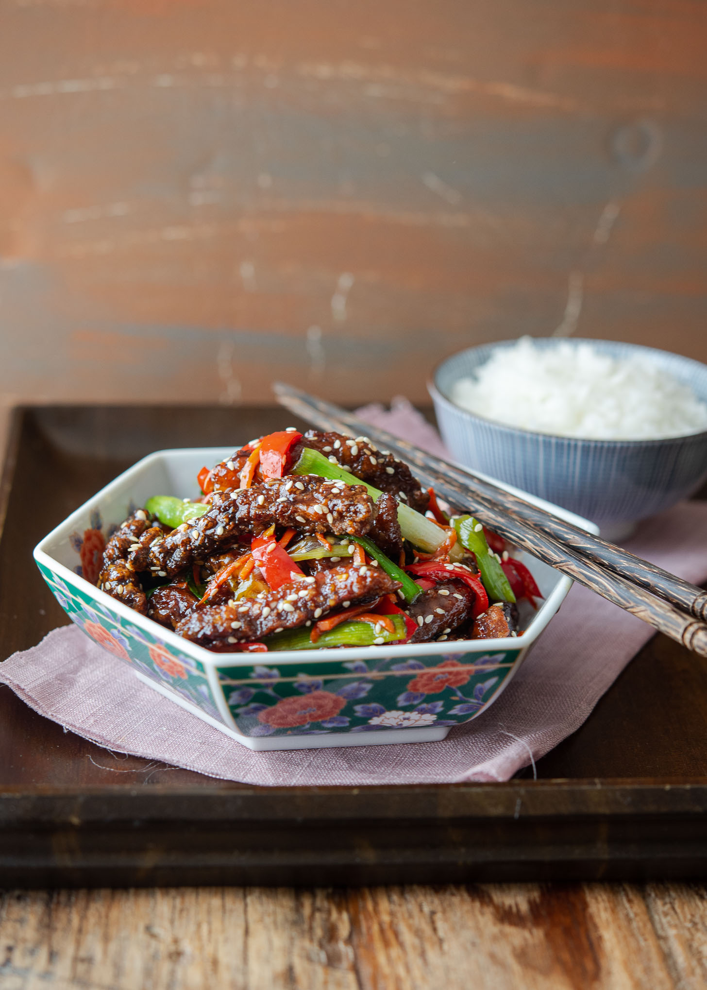 Chinese takeout style crispy beef is served with rice and chopsticks.