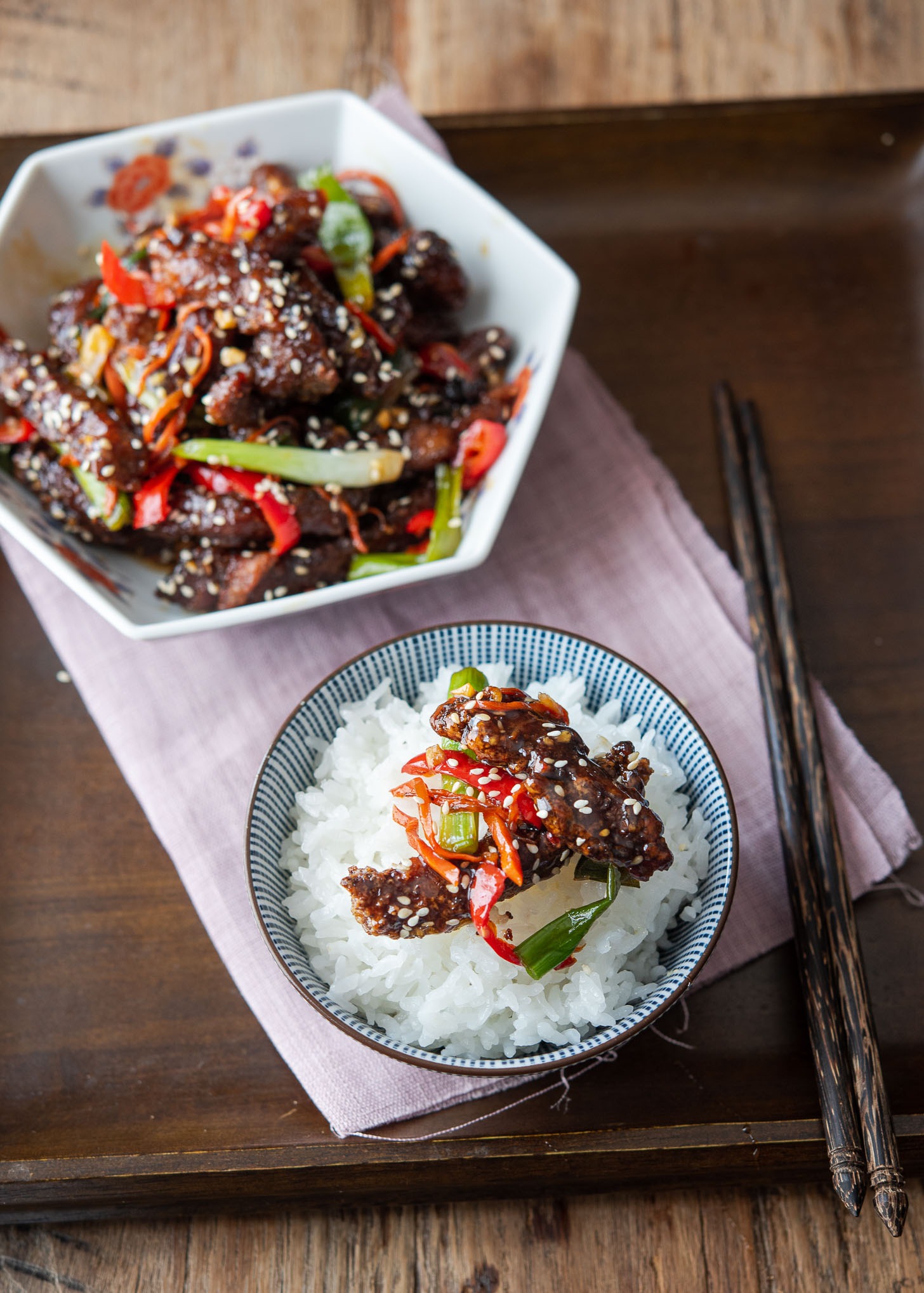 Crispy Chinese beef is served over a bowl of rice.
