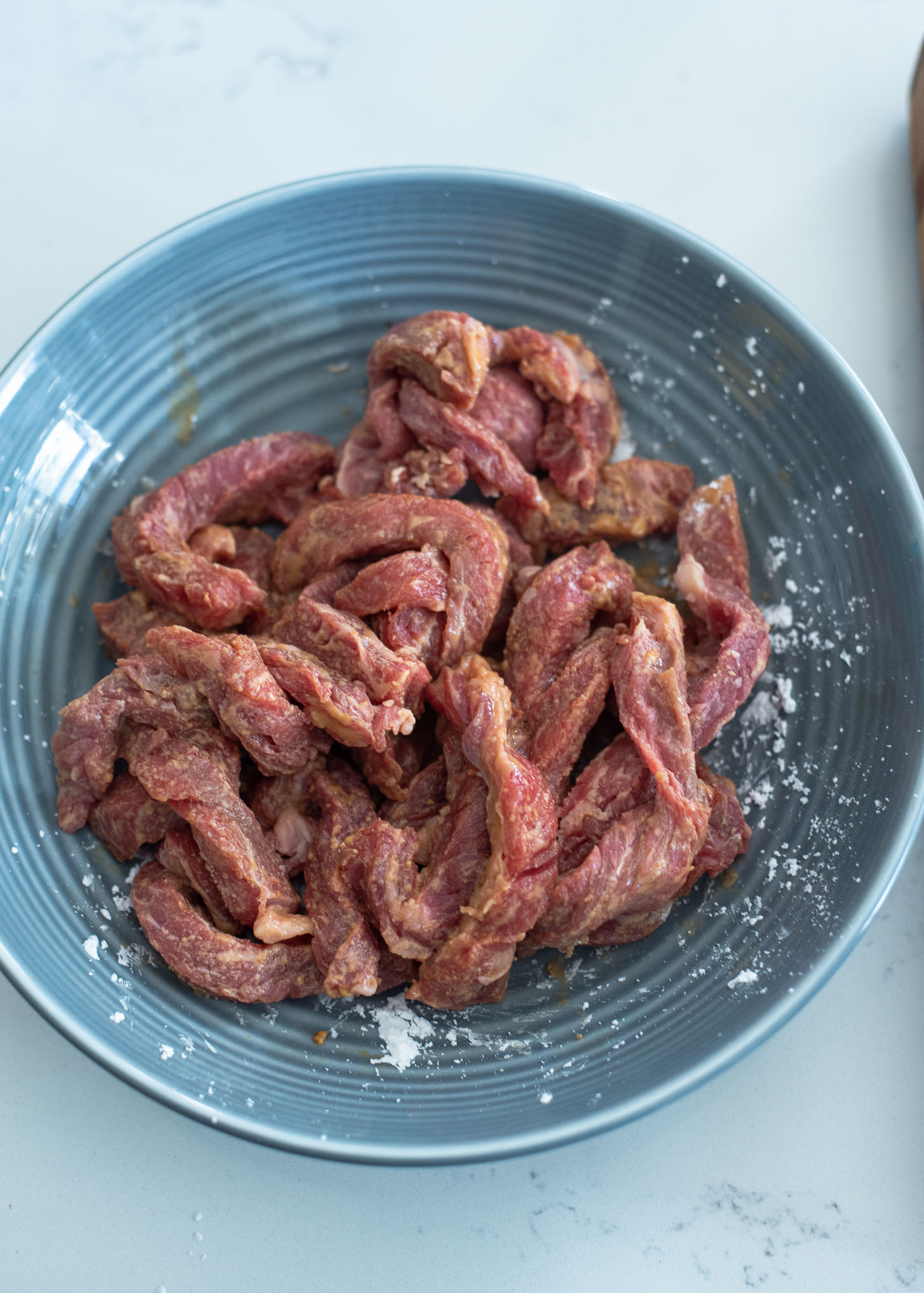 Beef strips for crispy beef are seasoned in a bowl.