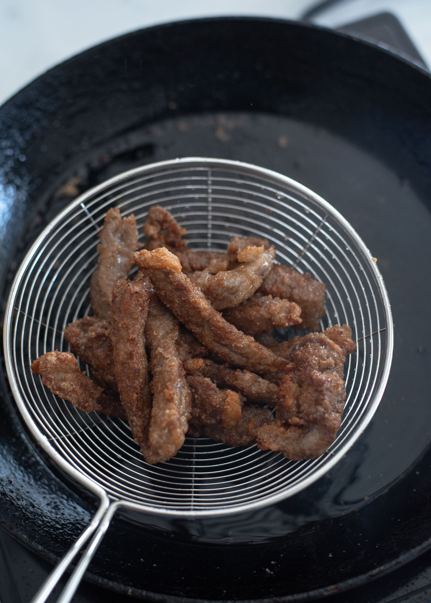 Double deep fried beed strips are drained from oil to make crispy beef.