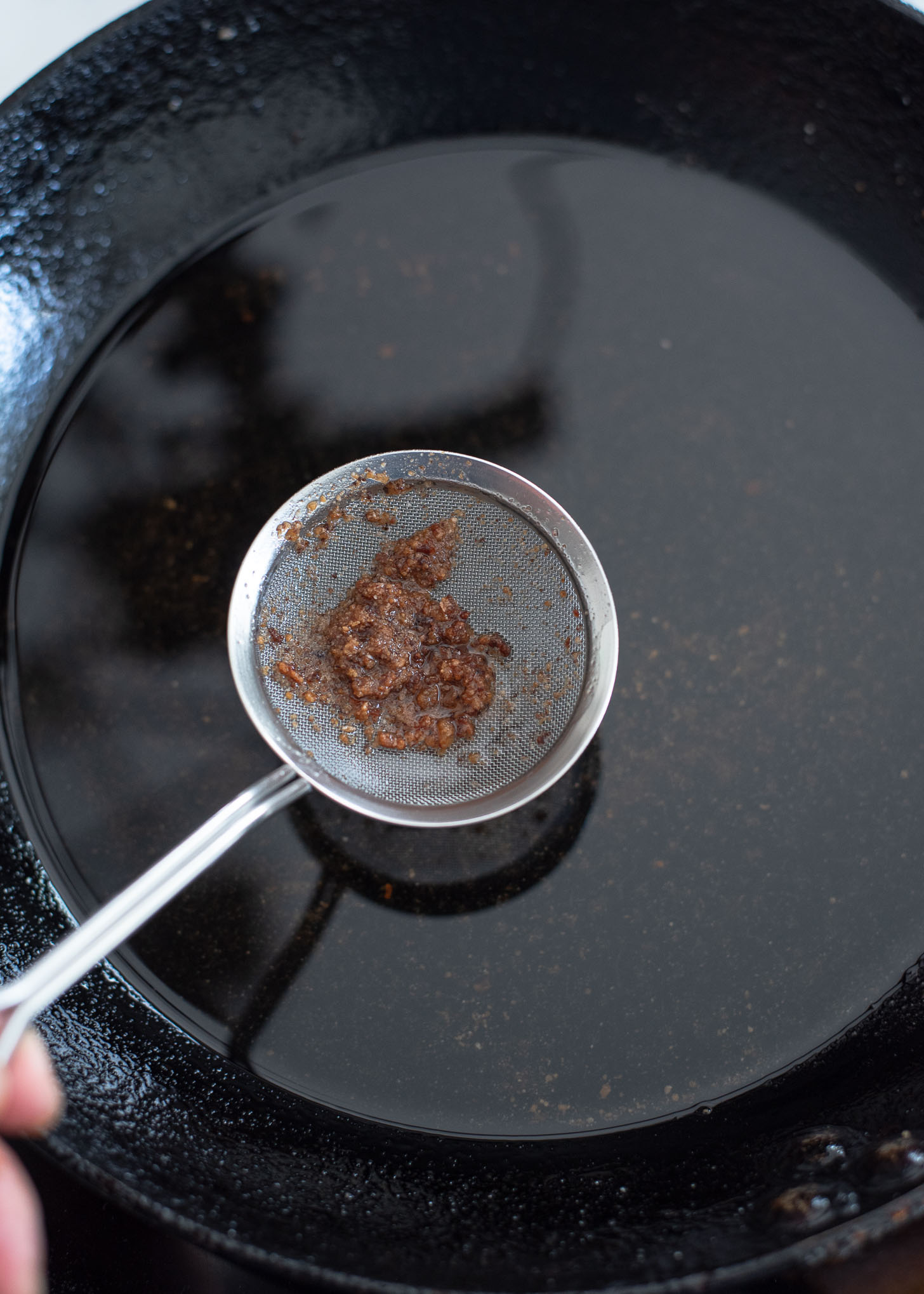 A fine skimmer is removing pieces of deep-fried remains from the oil.