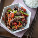 A bowl of Chinese crispy beef is served with rice on a tray