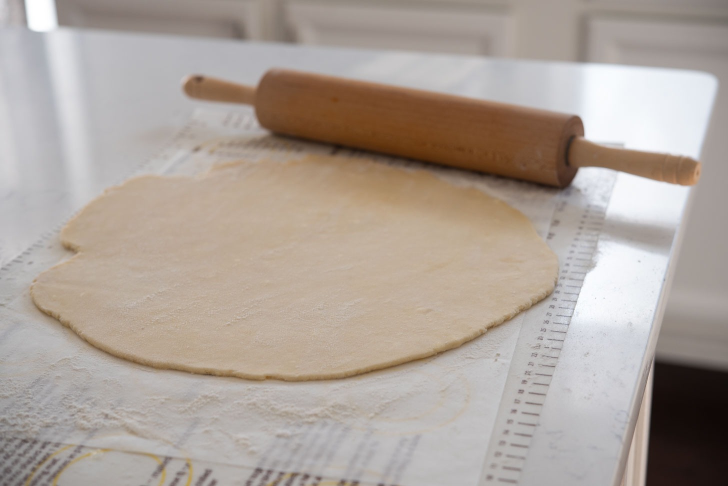 Homemade pie crust is rolled out with a rolling pin.