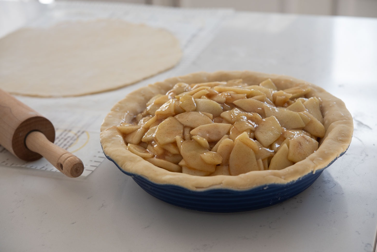 Cooked apple pie filling is placed on a pie crust in a pan.