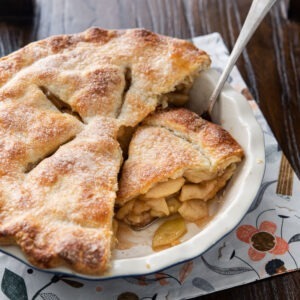 A piece of deep dish apple pie is sliced off from the entire pie in a pie dish.