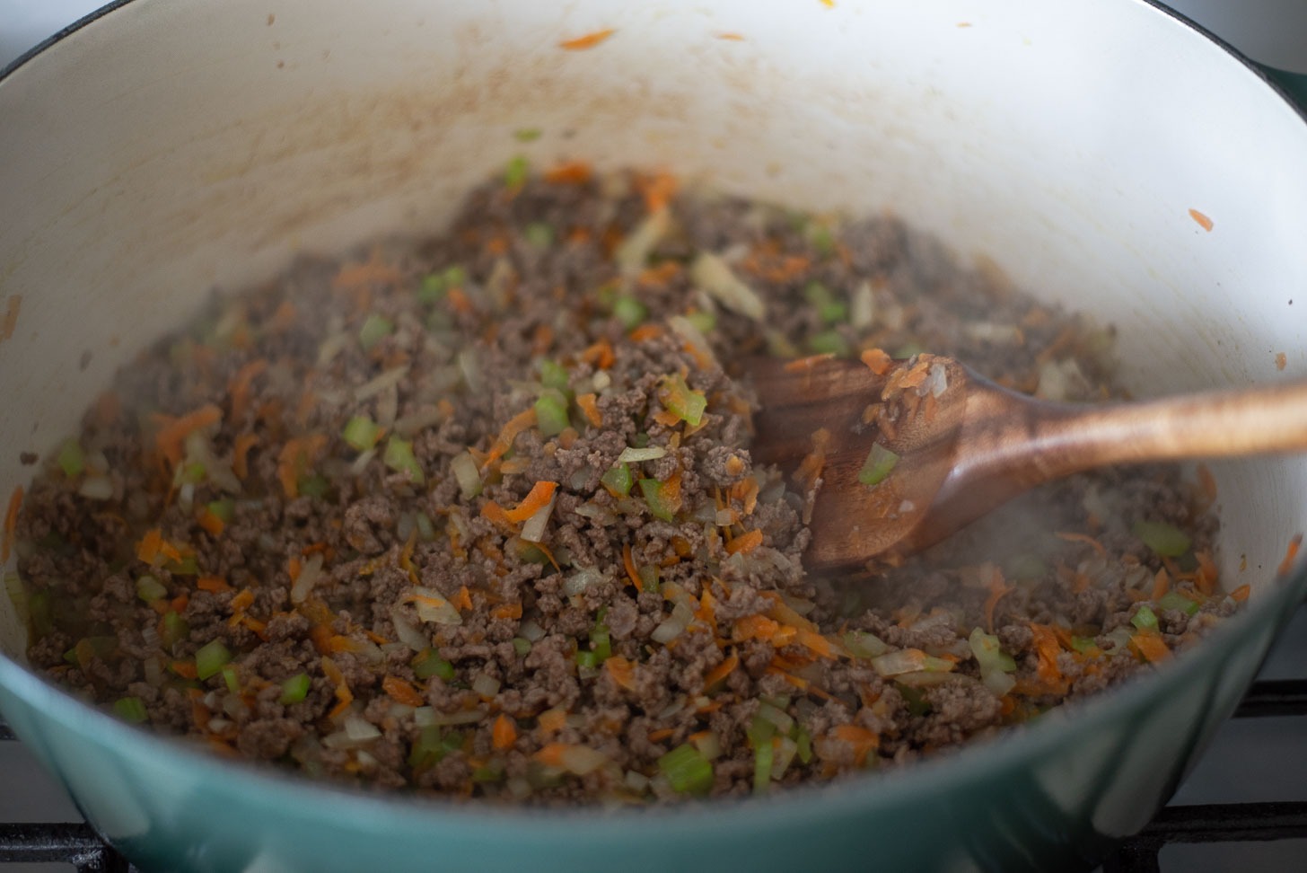 Onion, celery, carrot are added to browned ground beef to make homemade spaghetti sauce.