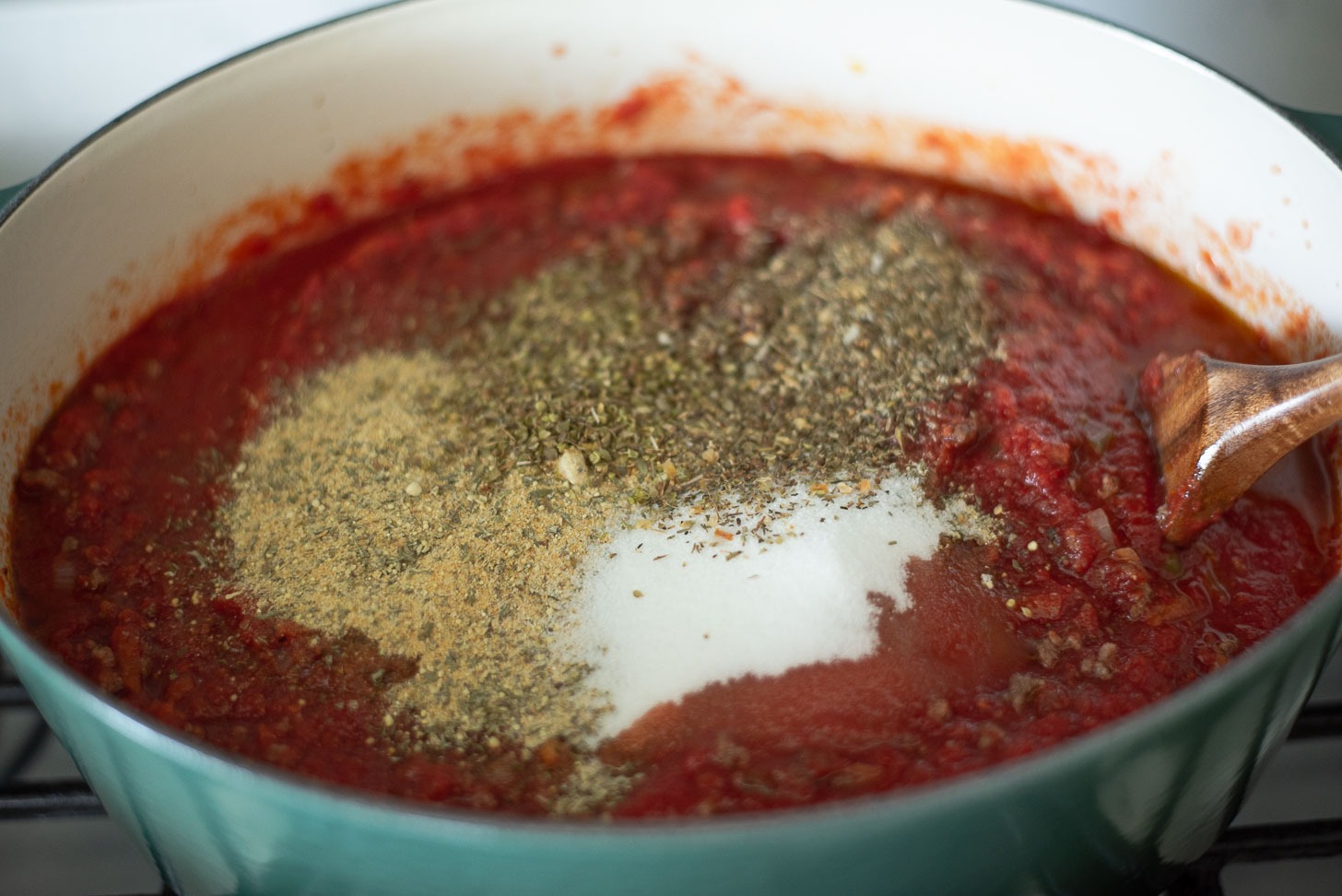 Canned crushed tomatoes and spices are added to beef and veggies in a pot.
