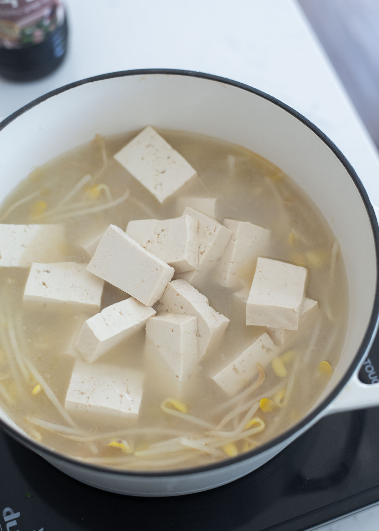 Soybean sprouts and tofu slices are added to pollock soup in a pot.
