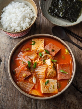 A bowl of kimchi jjigae made with Spam is served with rice and roasted seaweed.