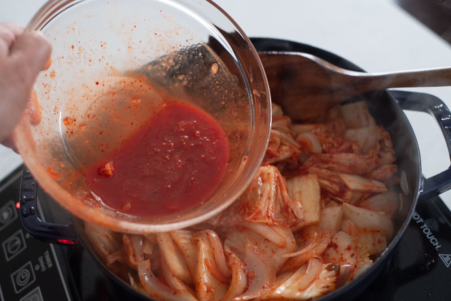 Kimchi juice is added to kimchi and onion mixture in the pot.