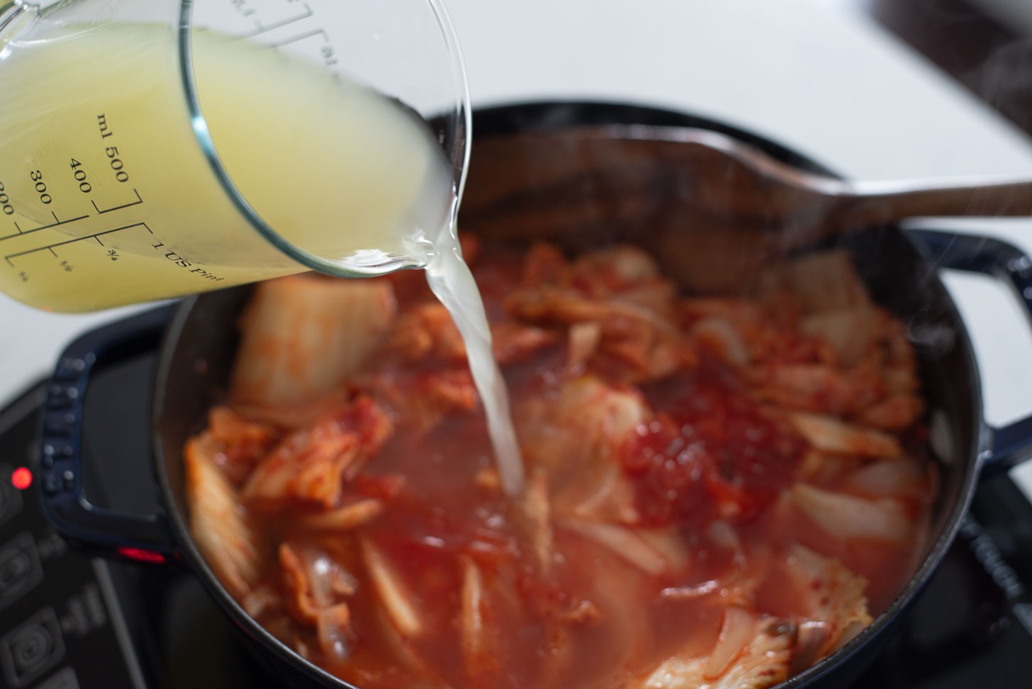 chicken stock is added to the kimchi onion mixture in a pot.