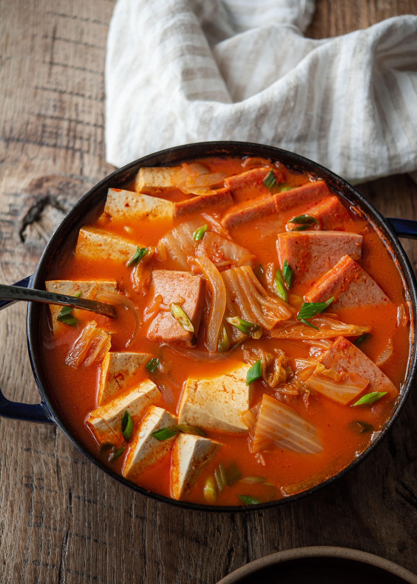 Kimchi jigae made with Spam and tofu are served in a pot.