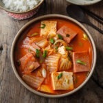 A bowl of kimchi jjigae made with Spam is served with rice and roasted seaweed.