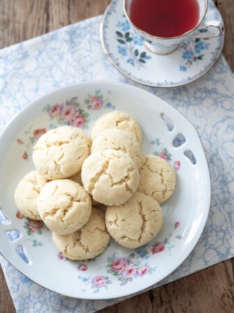 A plate of Swedish dream cookies are served with a cup of tea.