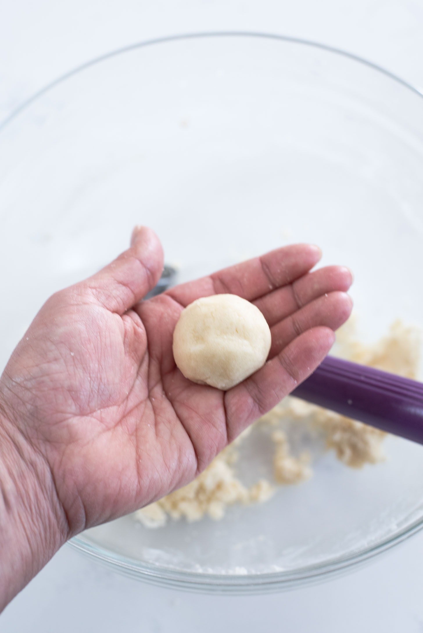 A cookie dough is formed into a ball in a hand.