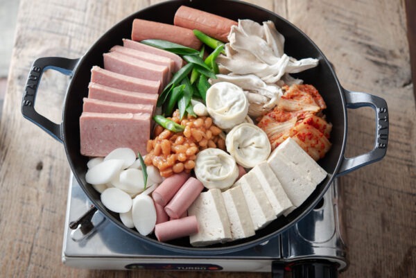 Budae jjigae ingredients are arranged in a pot over the portable stove.