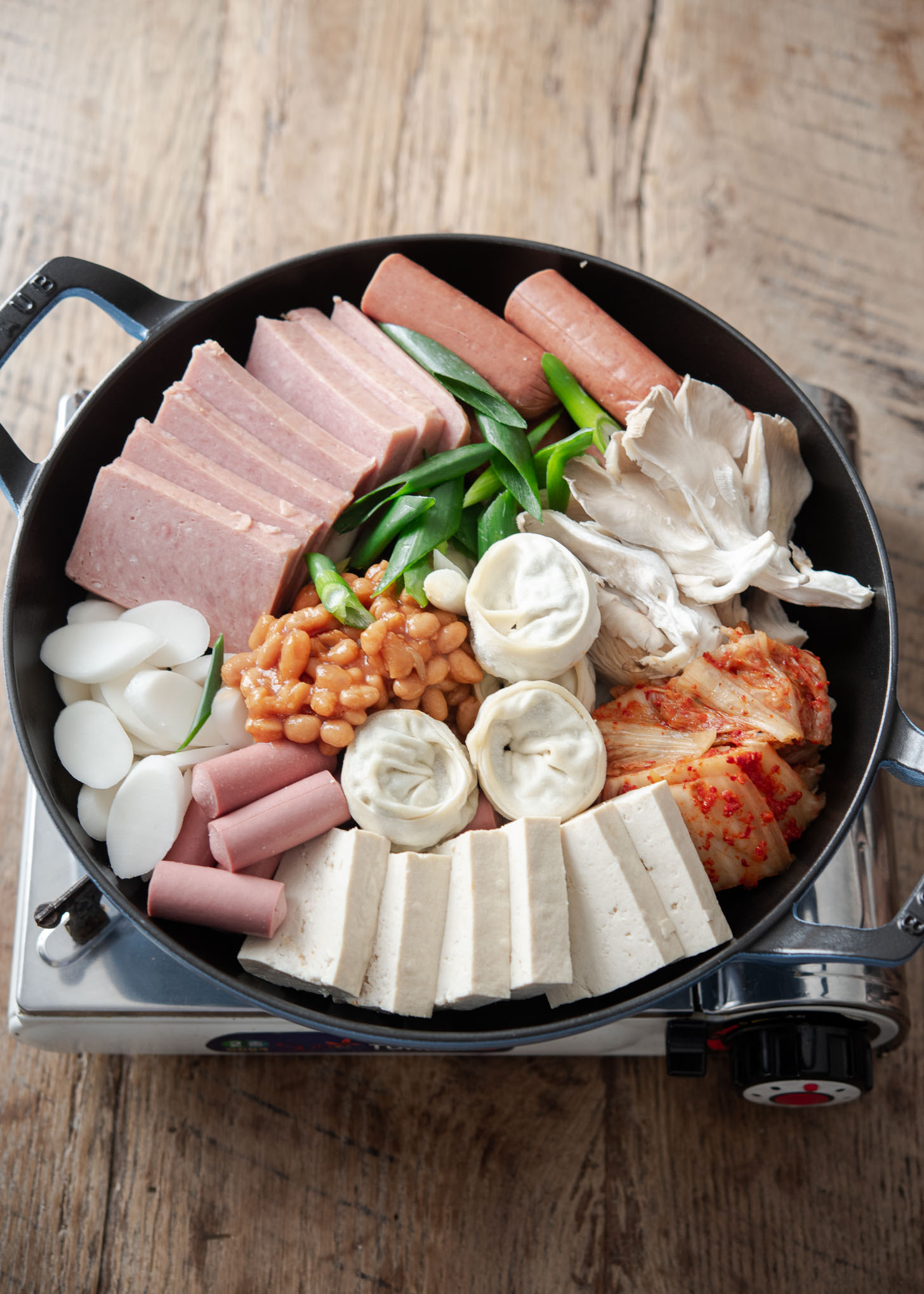 Army stew (Budae jjigae) ingredients are arranged in a pan.