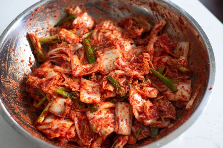 Salted cabbage pieces are tossed with kimchi paste in a large mixing bowl.