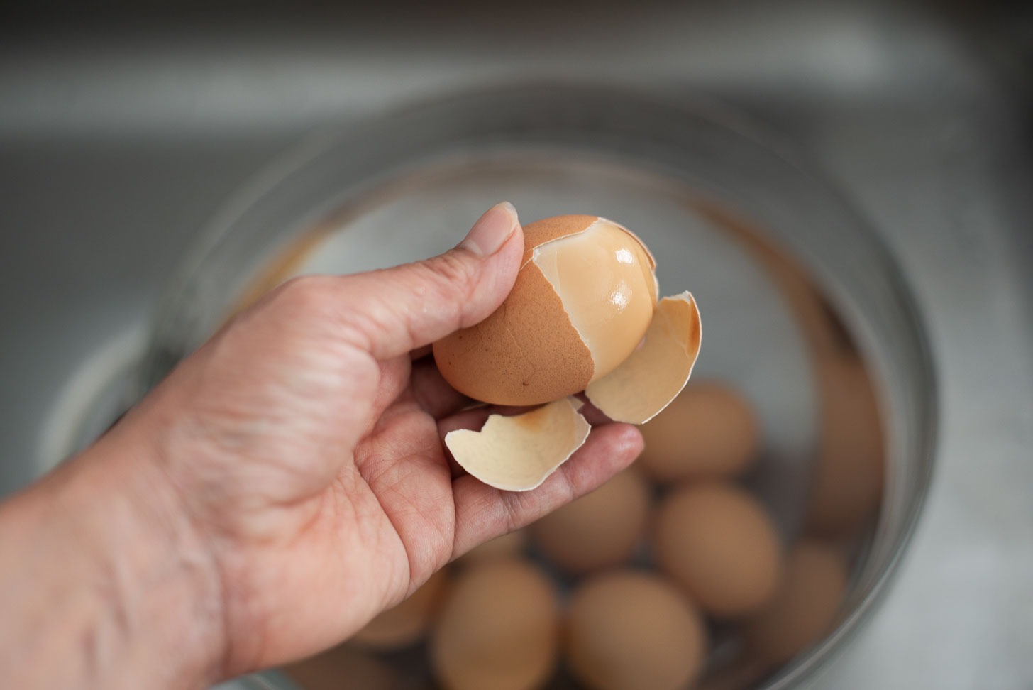 Peeling the egg shell off to reveal the brown egg whites of Korean sauna eggs.