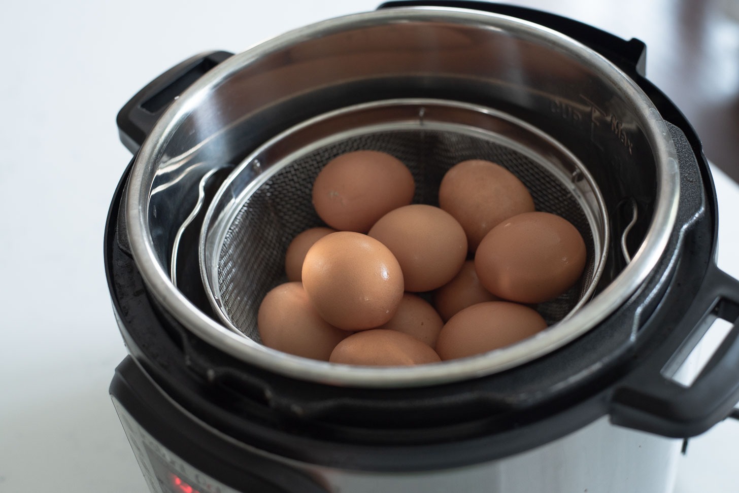 Brown eggs are placed in a mesh strainer inside the instant pot.