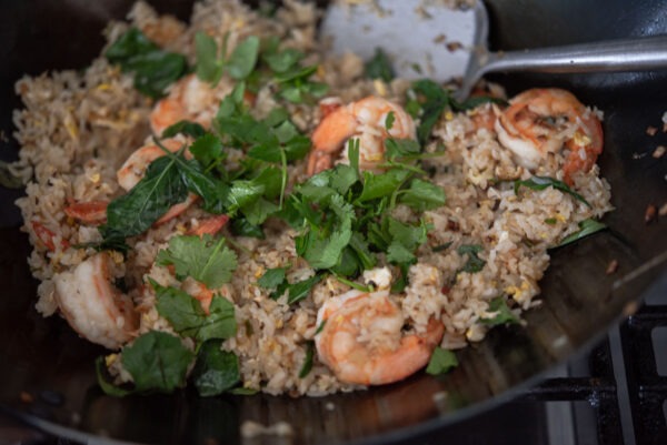 Thai basil is added to stir fried rice in a wok at last.