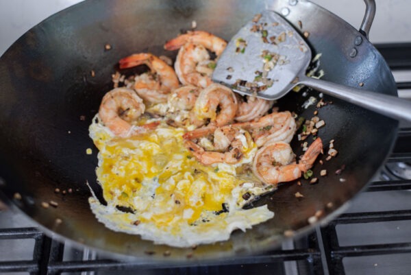 Eggs are stired fried next to shirmp mixture in a wok.